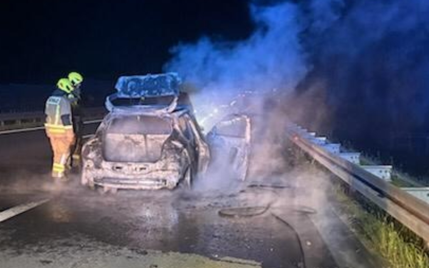 
        Spalony samochód na autostradzie, z dymem unoszącym się w powietrzu.
    