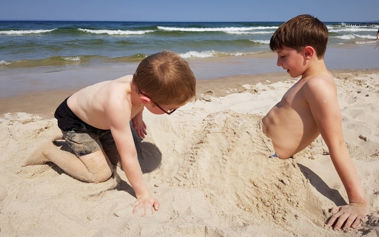 
        Dzieci bawiące się w piasku na plaży, radosne chwile.
    