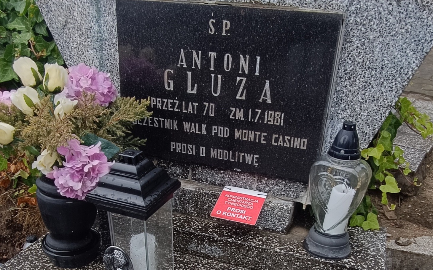 
        Nagrobek Antoniego Gluzy z kwiatami i lampionami.
    