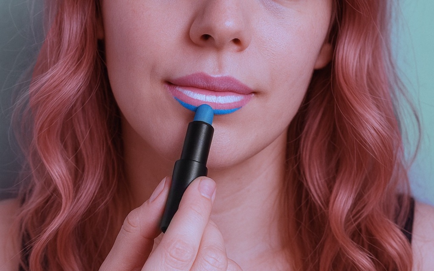 
        Kobieta malująca usta niebieską szminką, z różowymi włosami.
    