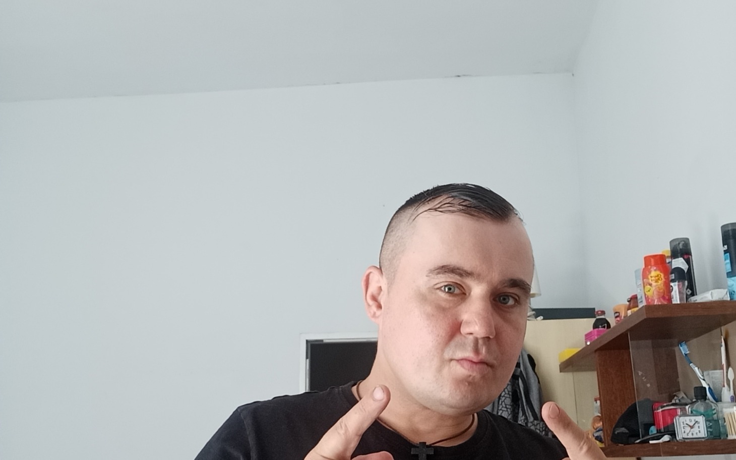 
        Mężczyzna w czarnym t-shircie, pozujący w swoim pokoju.
    