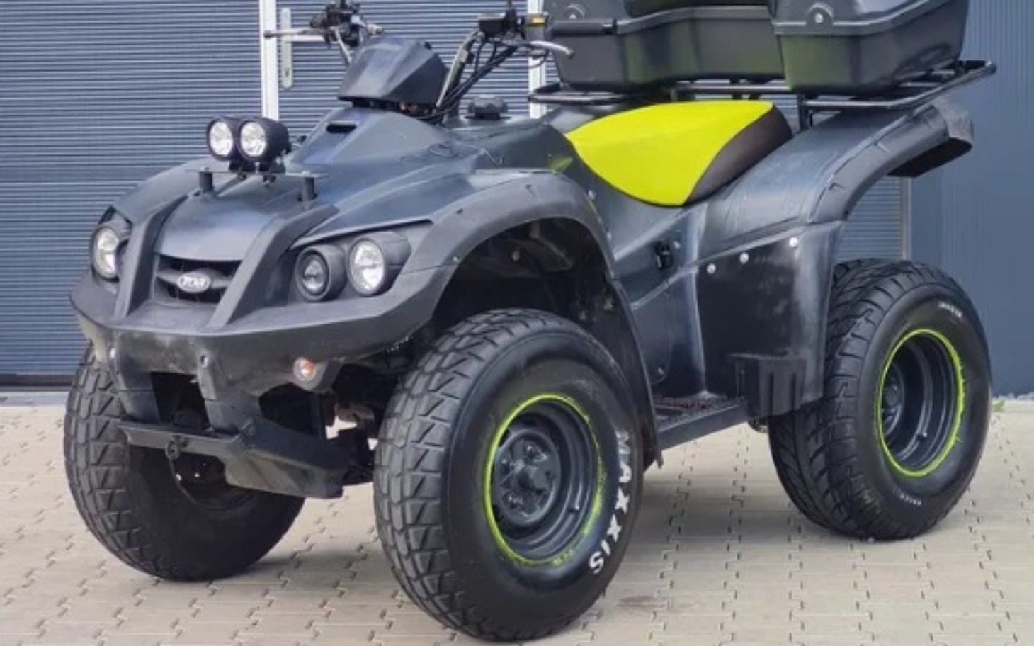 
        Quad w czarnym kolorze z zielonymi akcentami na tle garażu.
    