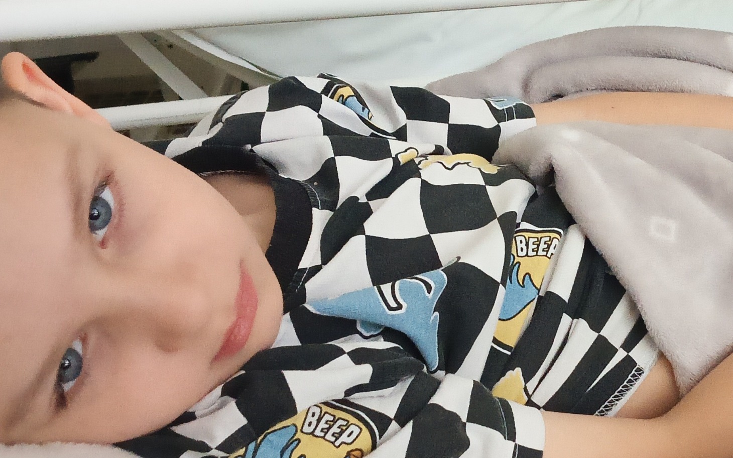 
        Chłopiec w łóżku, w koszulce w czarno-białą szachownicę.
    