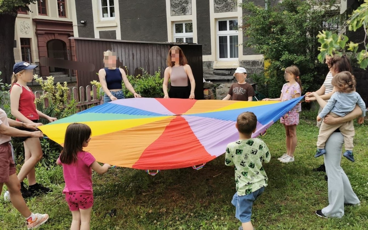 
        Dzieci bawiące się z kolorowym parasolem w ogrodzie.
    