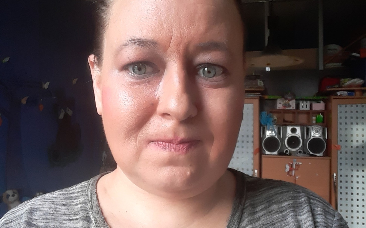 
        Portret kobiety z jasnymi oczami, uśmiechającej się w domowym otoczeniu.
    