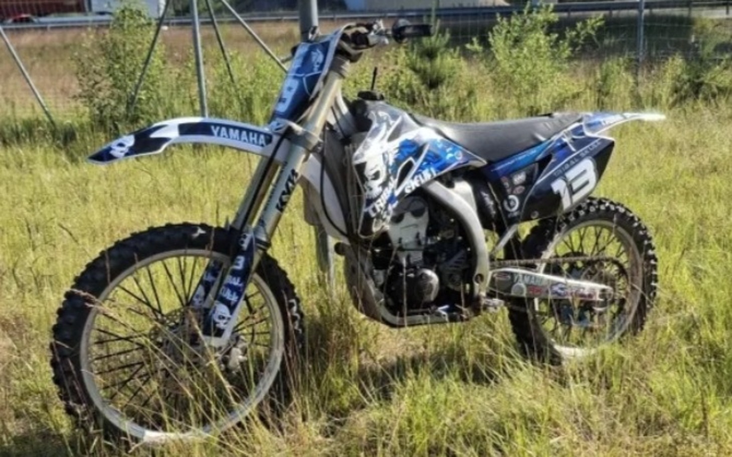 
        Motocykl terenowy na tle trawy, gotowy do jazdy.
    