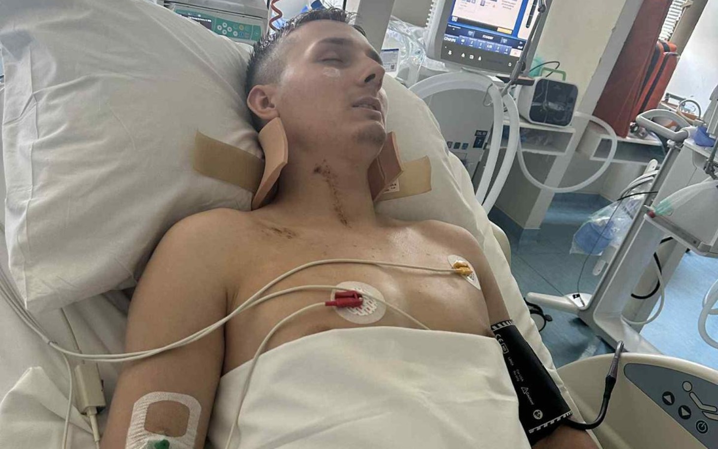 
        Młody mężczyzna leżący w szpitalnym łóżku, z raną na szyi.
    