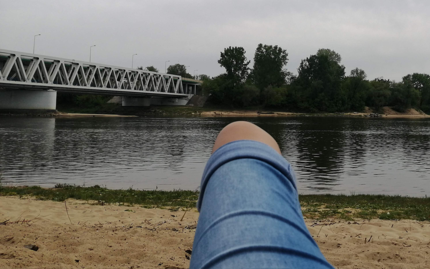 
        Widok na rzekę z plaży, z mostem w tle.
    