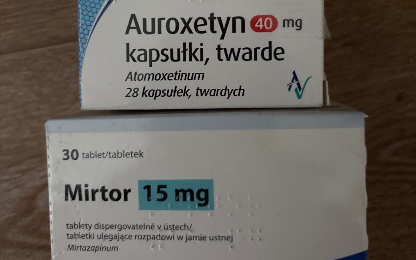 
        Opakowania leków Auroxetyn i Mirtor na drewnianym tle.
    