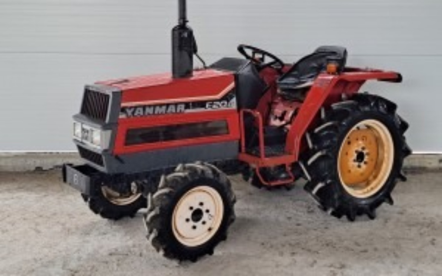 
        Czerwony traktor Yanmar na tle białej ściany.
    