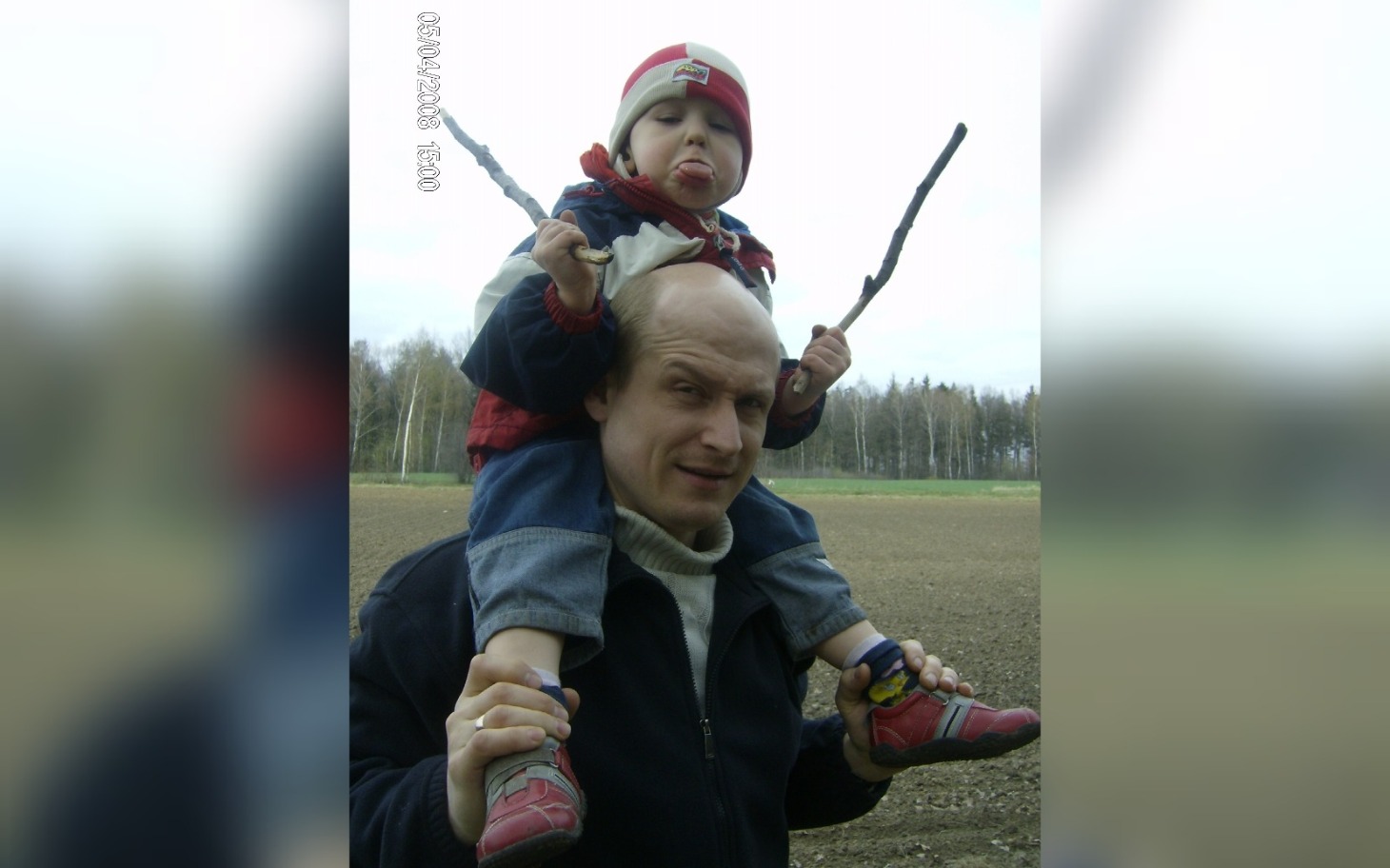 
        Dziecko na plecach ojca, trzymające patyki i robiące miny.
    