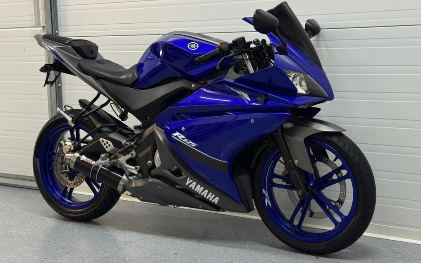 
        Niebieski motocykl sportowy zaparkowany w garażu.
    