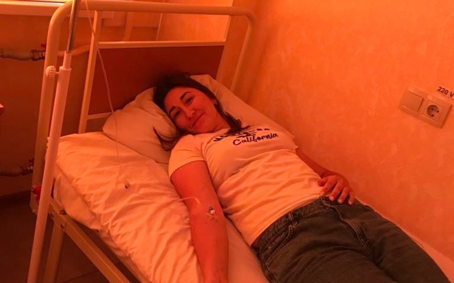 
        Kobieta leżąca na łóżku szpitalnym, uśmiechająca się.
    