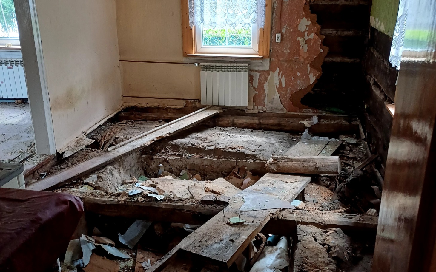 
        Zniszczone wnętrze domu z odsłoniętymi podłogami i uszkodzeniami ścian.
    