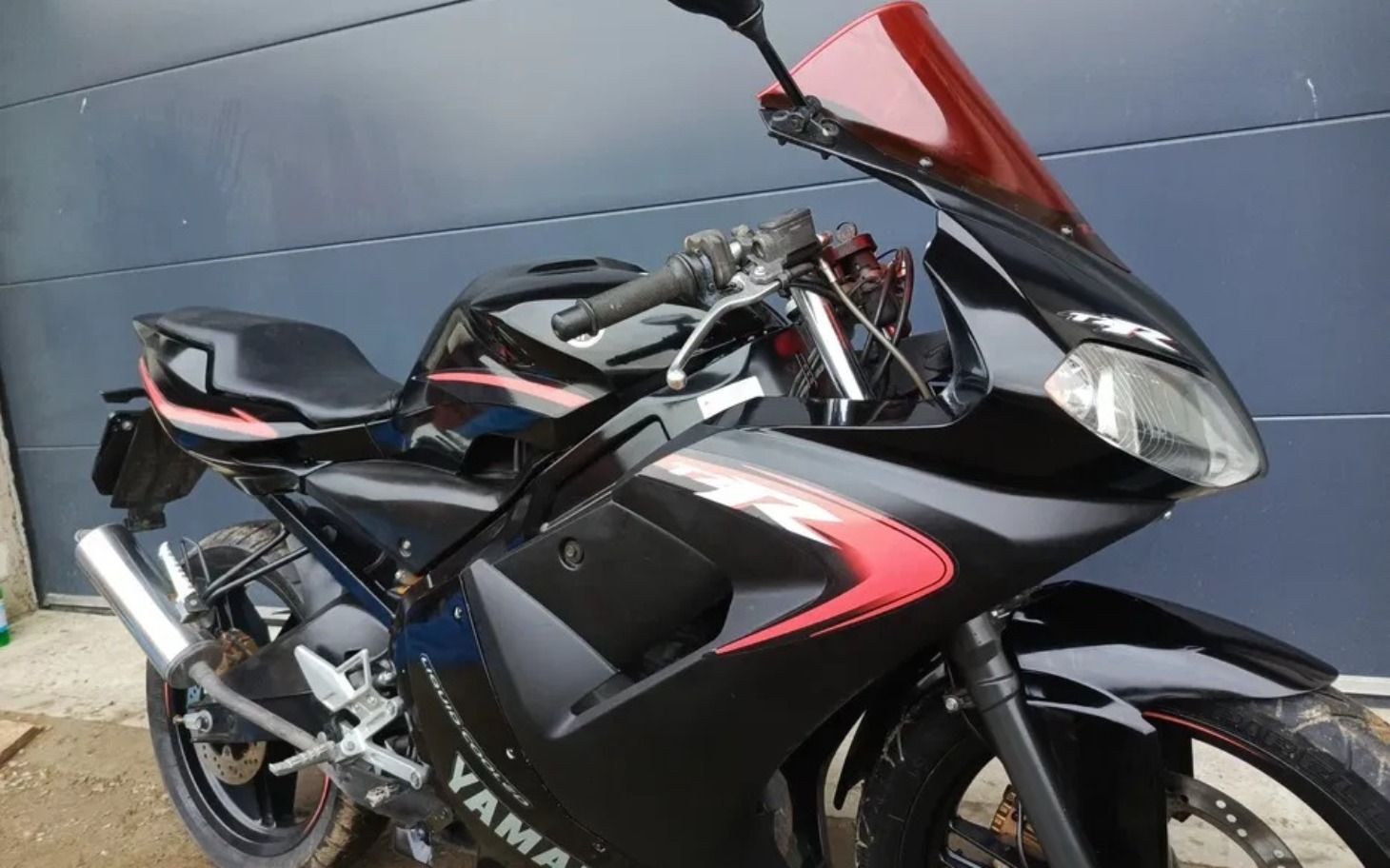 
        Czarny motocykl sportowy zaparkowany na tle szarej ściany.
    