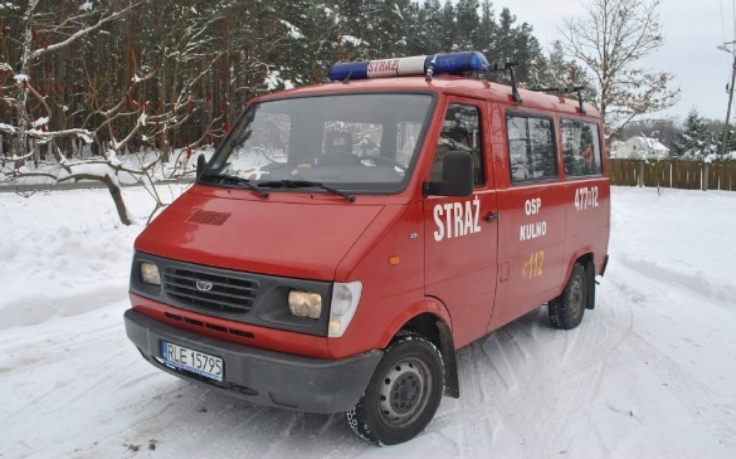 
        Czerwony wóz strażacki na tle zimowego krajobrazu.
    