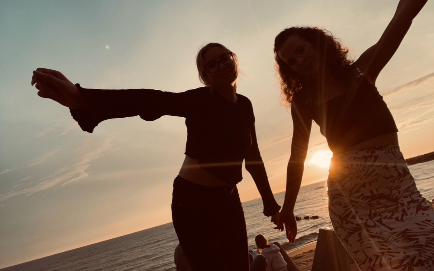
        Dwie kobiety tańczące na plaży podczas zachodu słońca.
    