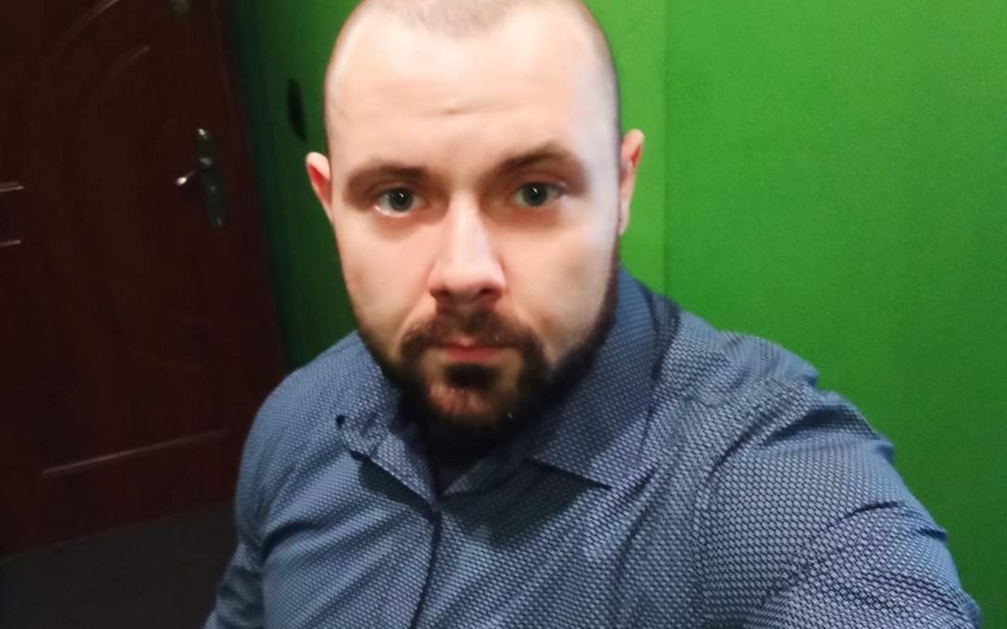 
        Mężczyzna w niebieskiej koszuli na tle zielonej ściany.
    