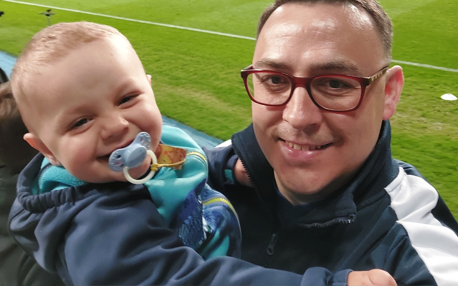 
        Uśmiechnięty chłopiec trzymający się za szyję dorosłego mężczyzny.
    