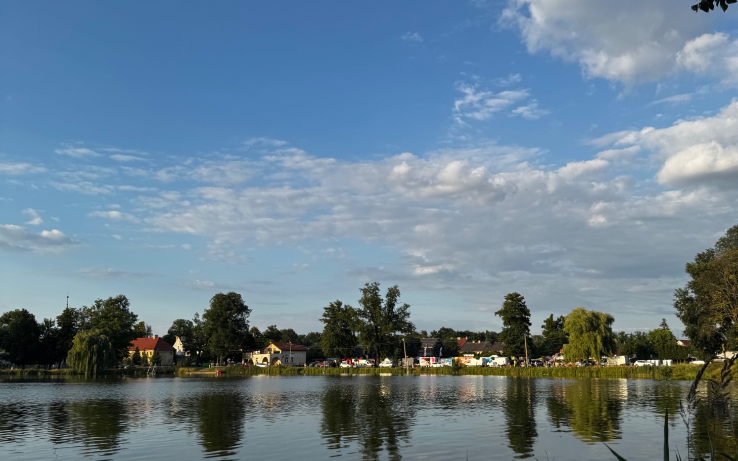 
        Widok na jezioro z chmurami i drzewami w tle.
    