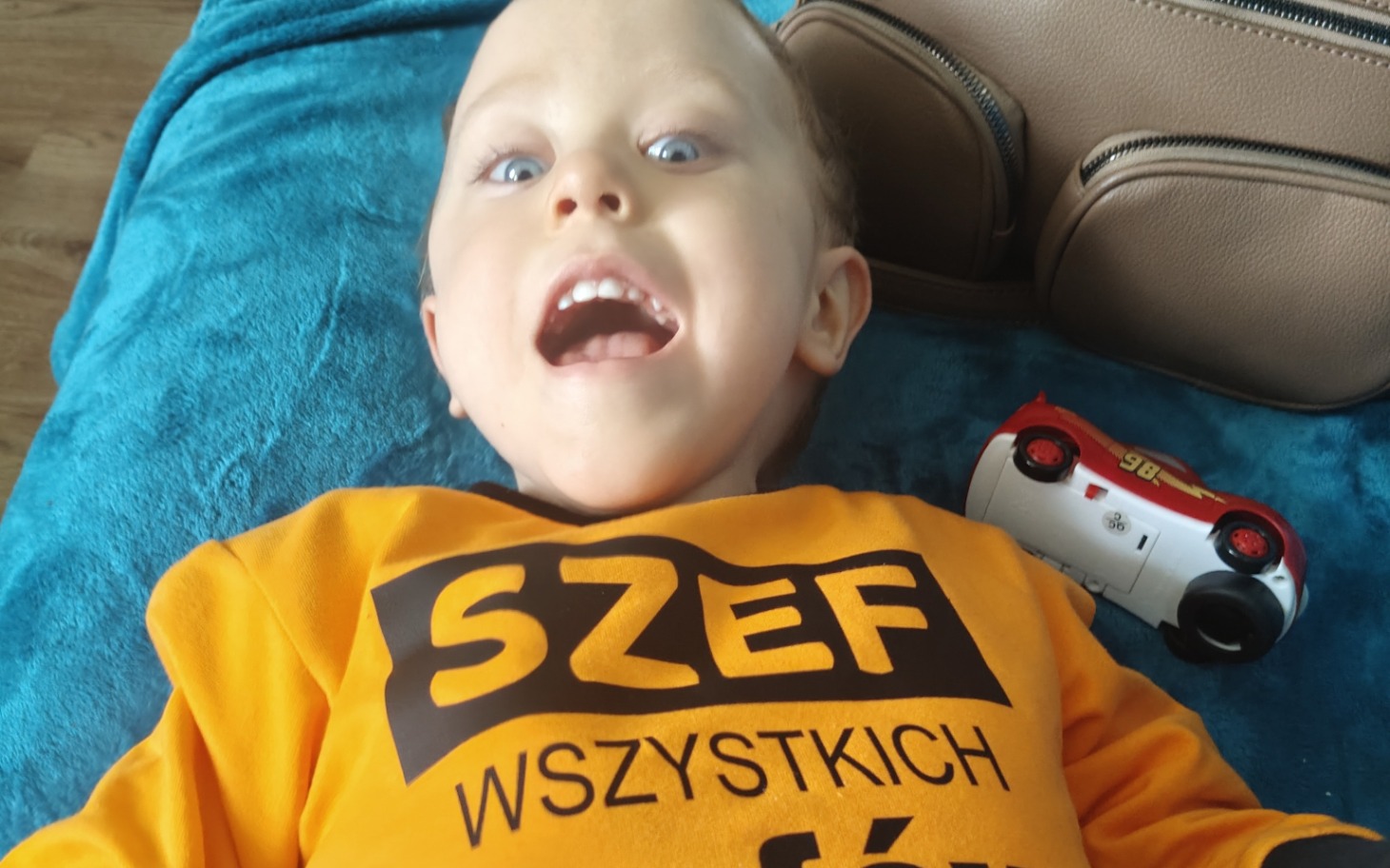 
        Mały chłopiec w pomarańczowej koszulce, uśmiechający się do kamery.
    