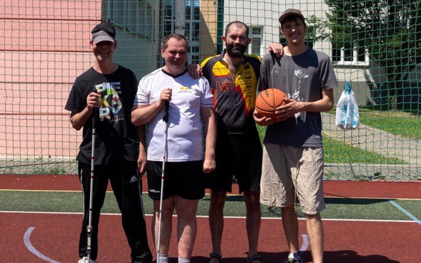 
        Czterech mężczyzn pozujących na boisku sportowym z piłką koszykową.
    