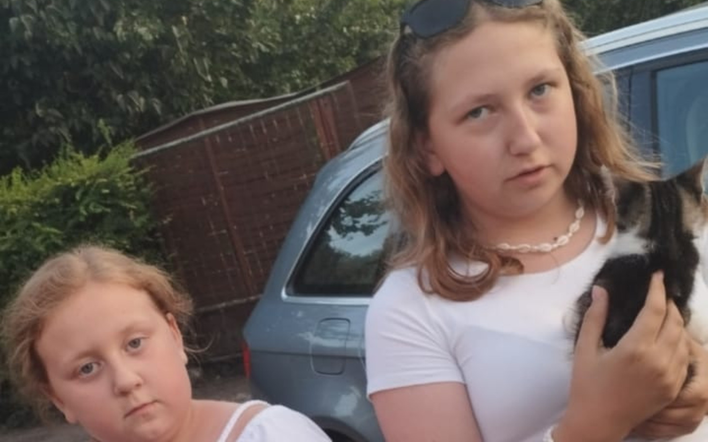 
        Dwie dziewczynki pozują z kotem, wyglądają poważnie.
    