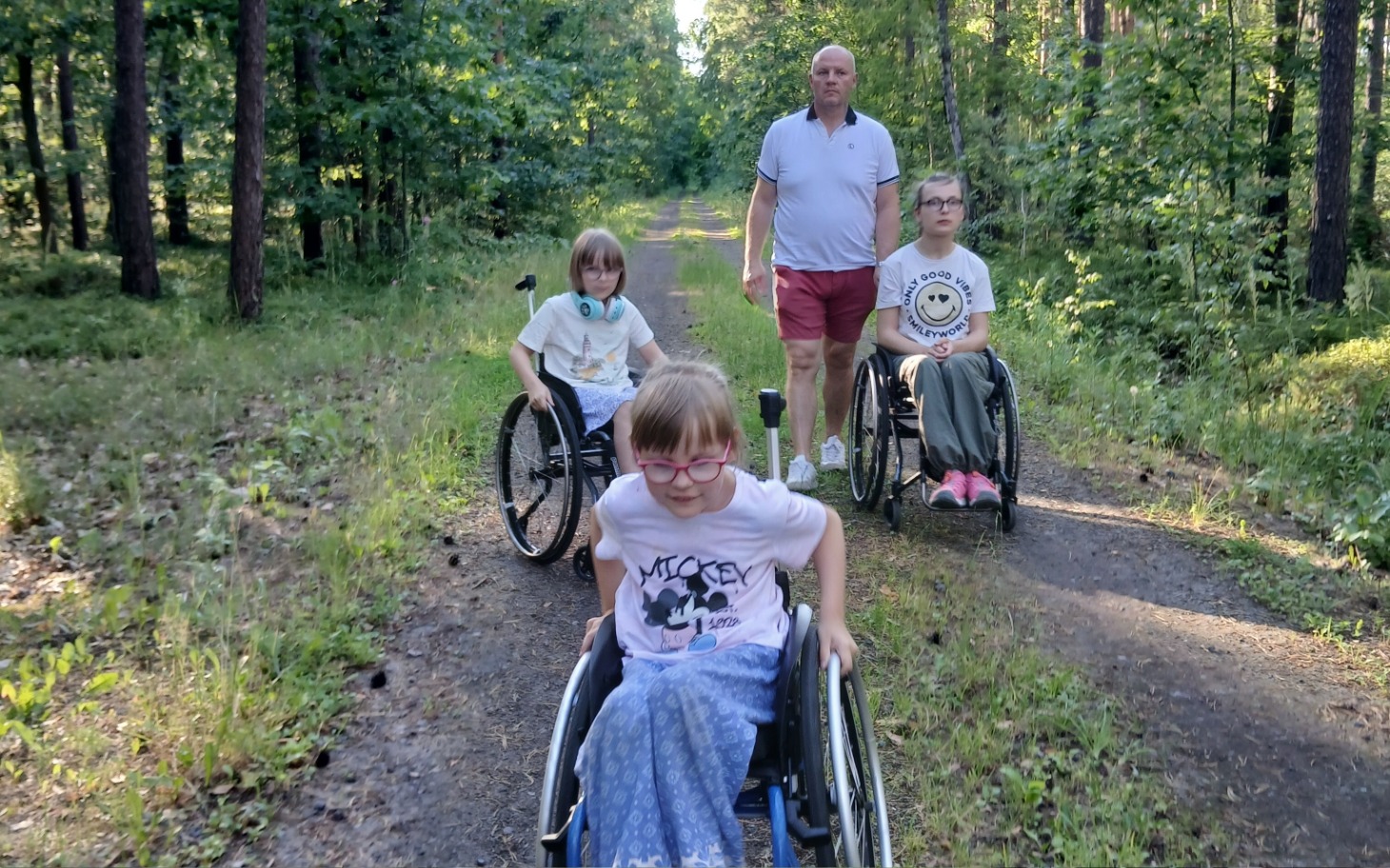
        Czwórka dzieci na wózkach inwalidzkich w lesie.
    