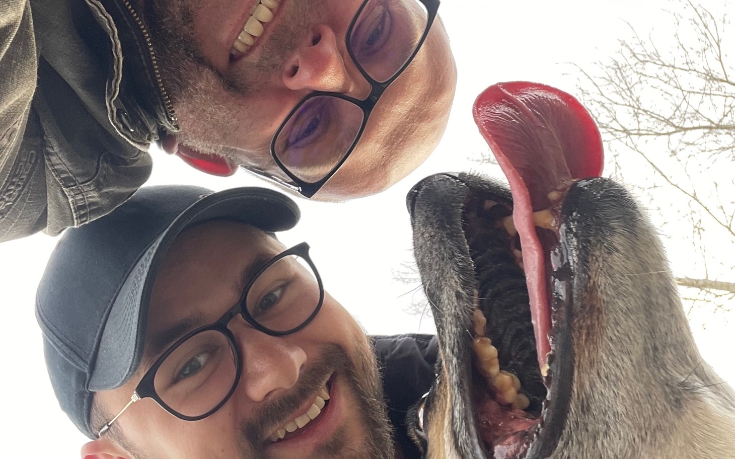 
        Dwóch mężczyzn uśmiecha się z psem, pokazując radość.
    