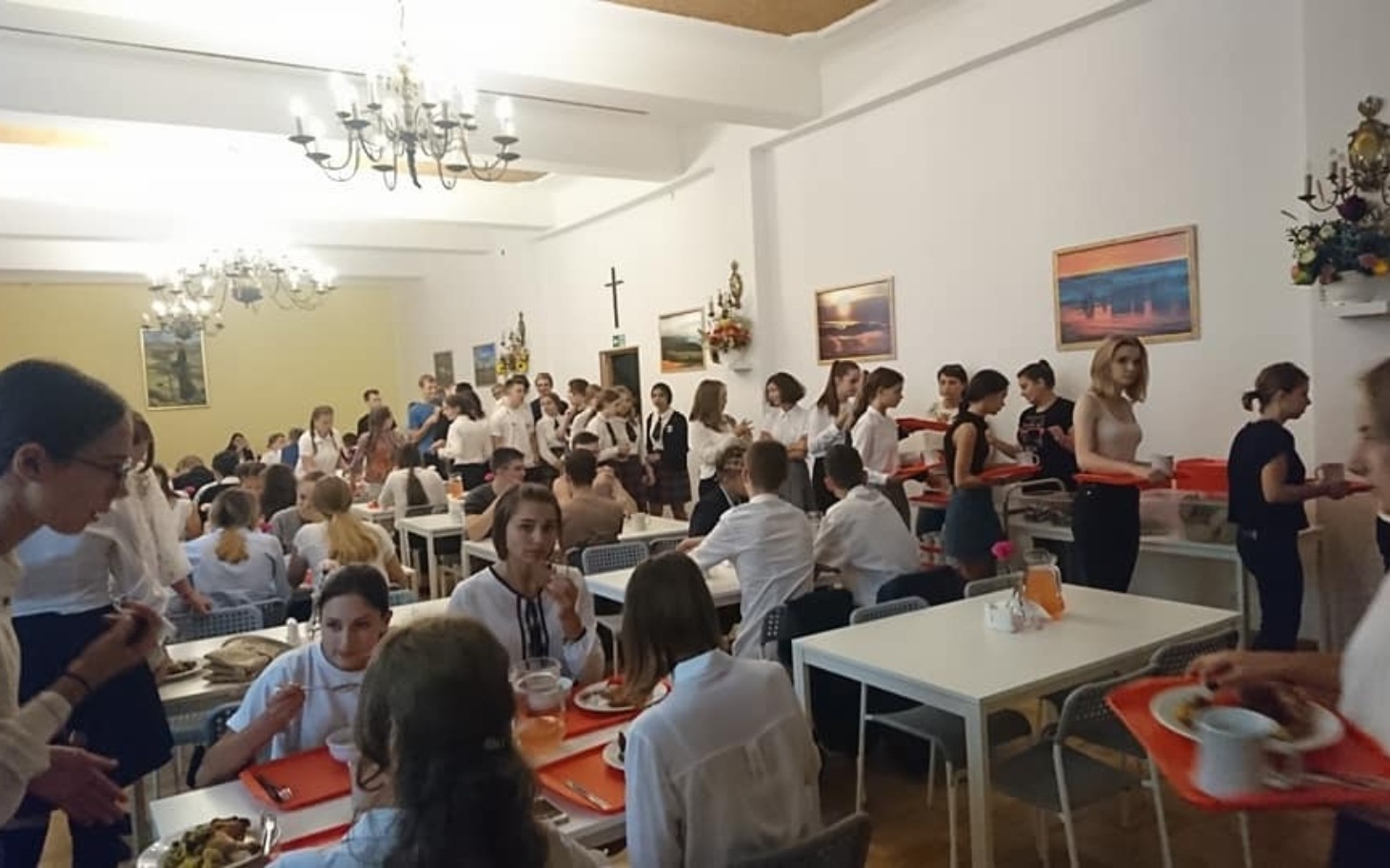 
        Zatłoczona stołówka z uczniami jedzącymi posiłki.
    