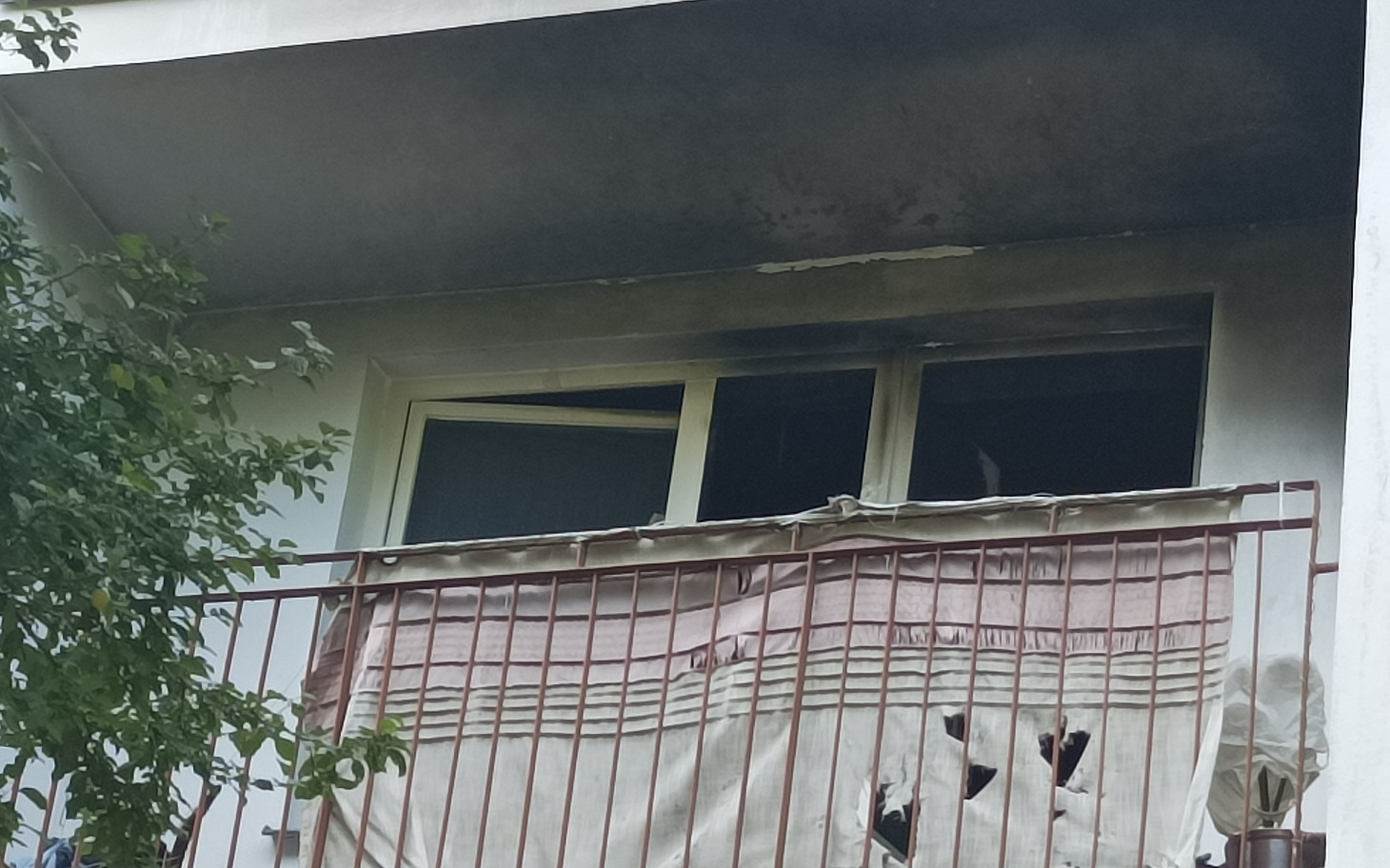 
        Zniszczony balkon z uszkodzonymi oknami i zasłoną.
    