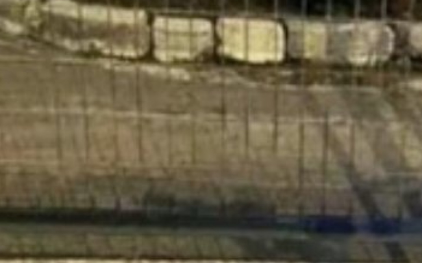 
        Fragment ogrodzenia z widocznymi kamieniami na ziemi.
    