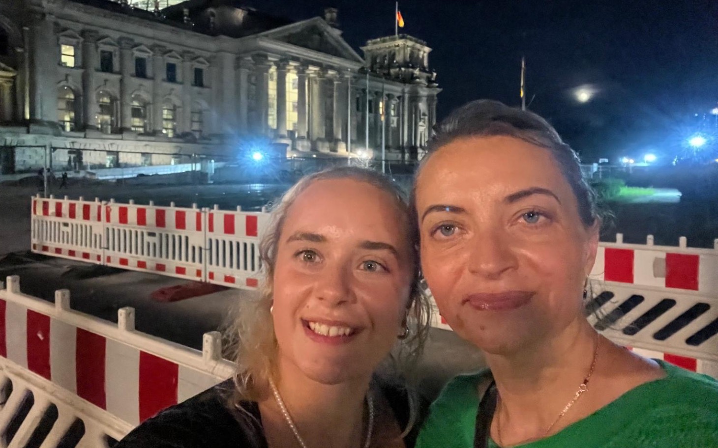 
        Dwie kobiety na tle budynku rządowego w Berlinie nocą.
    