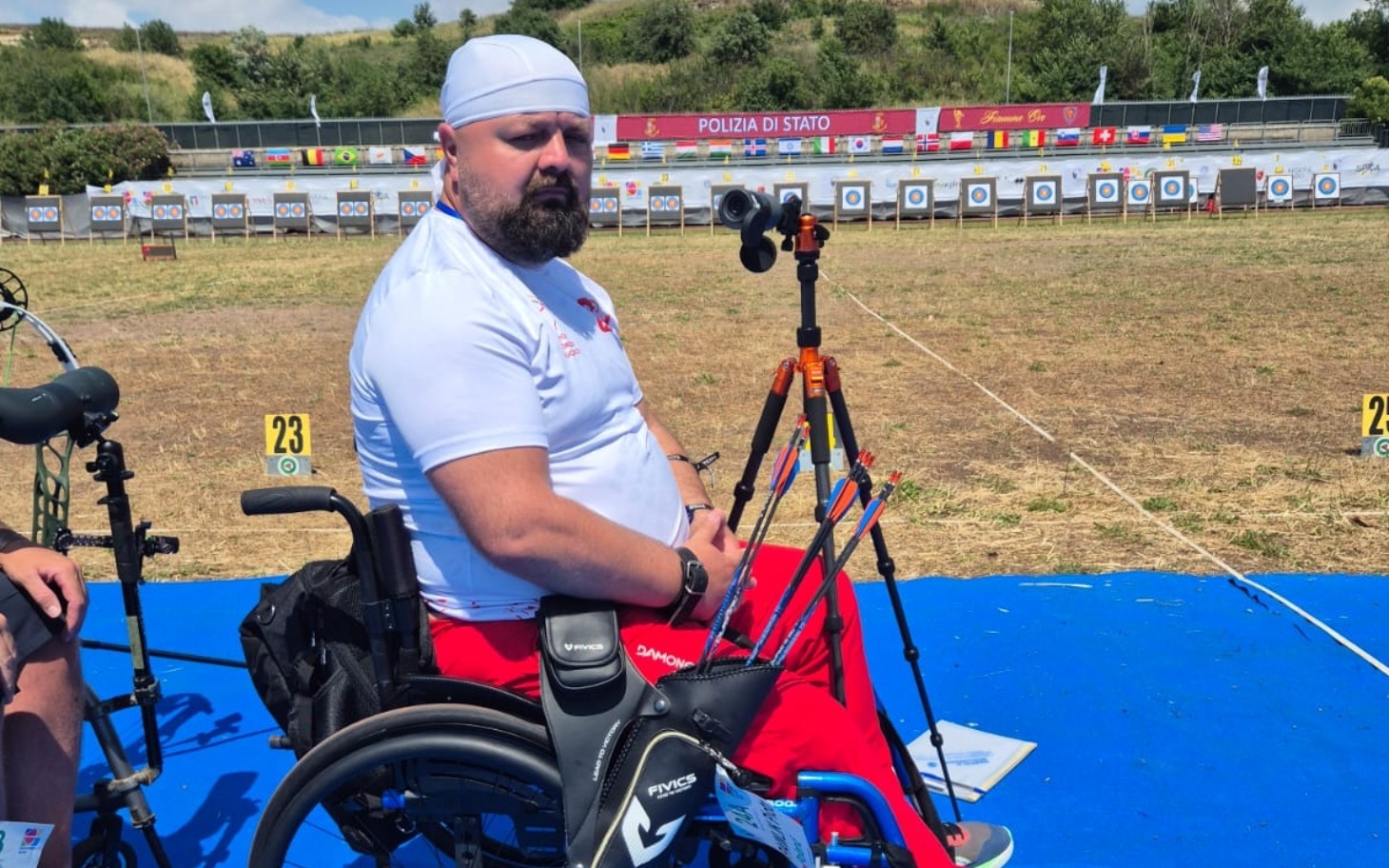 
        Mężczyzna na wózku inwalidzkim, przygotowujący się do strzelania.
    