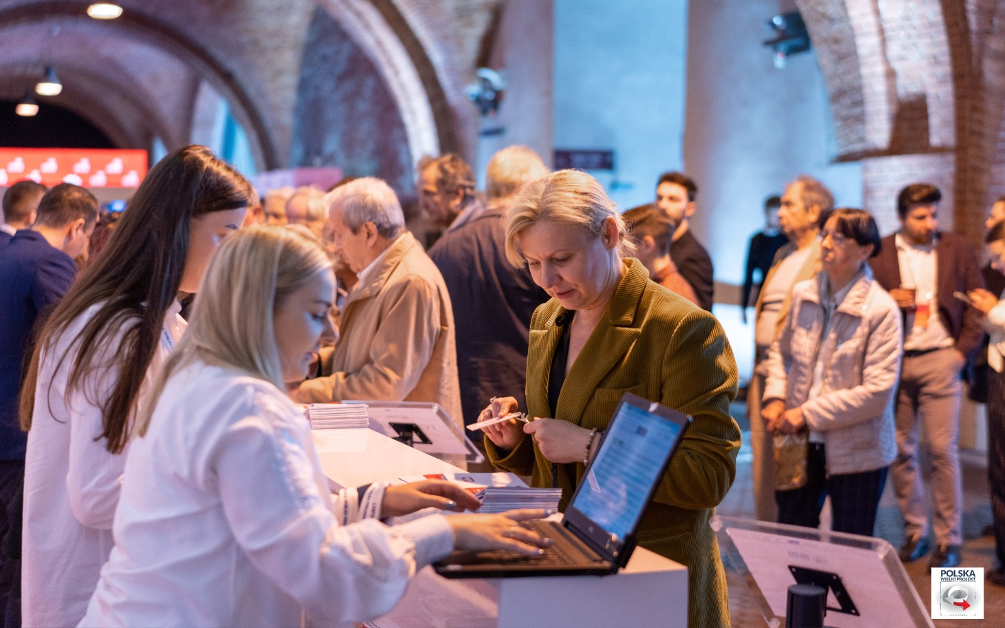 
        Uczestnicy wydarzenia rozmawiają przy stoisku informacyjnym.
    