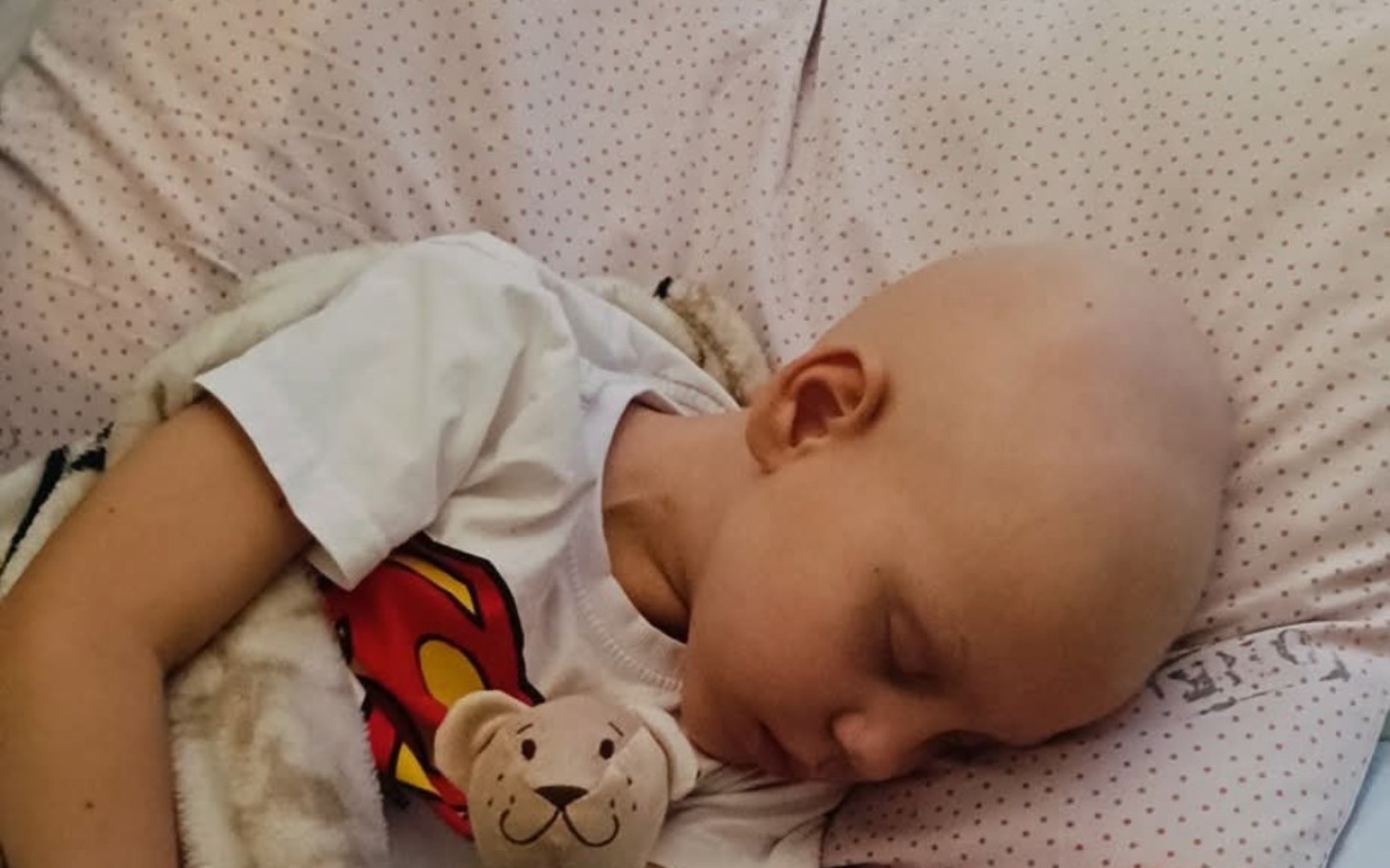 
        Mały chłopiec śpiący z pluszowym misiem, bez włosów.
    