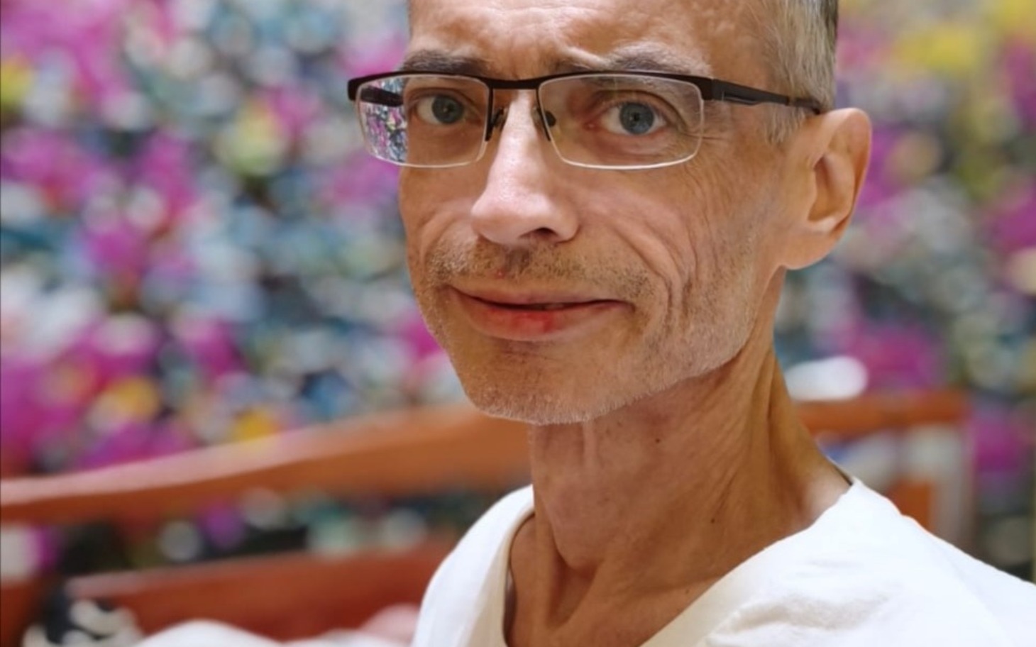 
        Mężczyzna w okularach, uśmiechający się na tle kolorowej ściany.
    