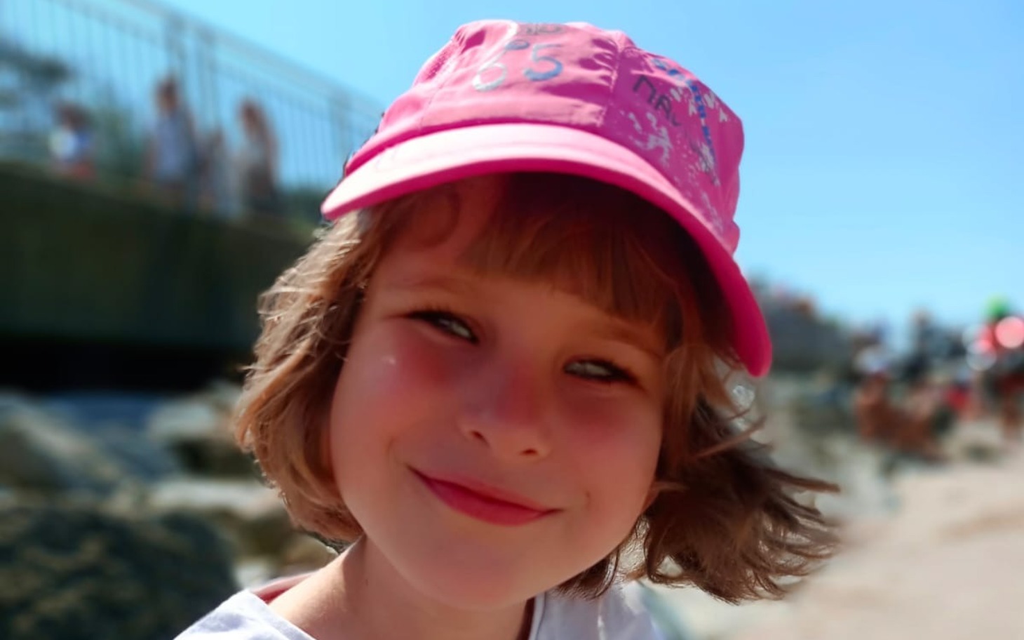 
        Uśmiechnięta dziewczynka w różowej czapce, na tle plaży.
    
