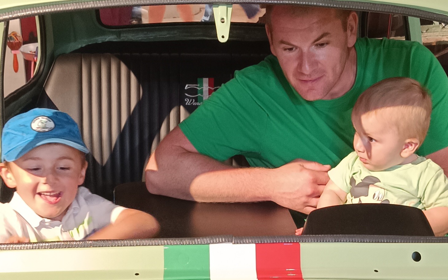 Dzieci bawiące się w samochodzie z dorosłym, uśmiechnięte.