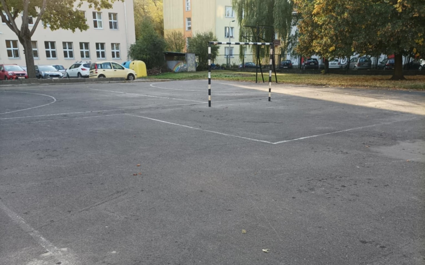 Pusty plac zabaw z boiskami, otoczony drzewami i budynkami.