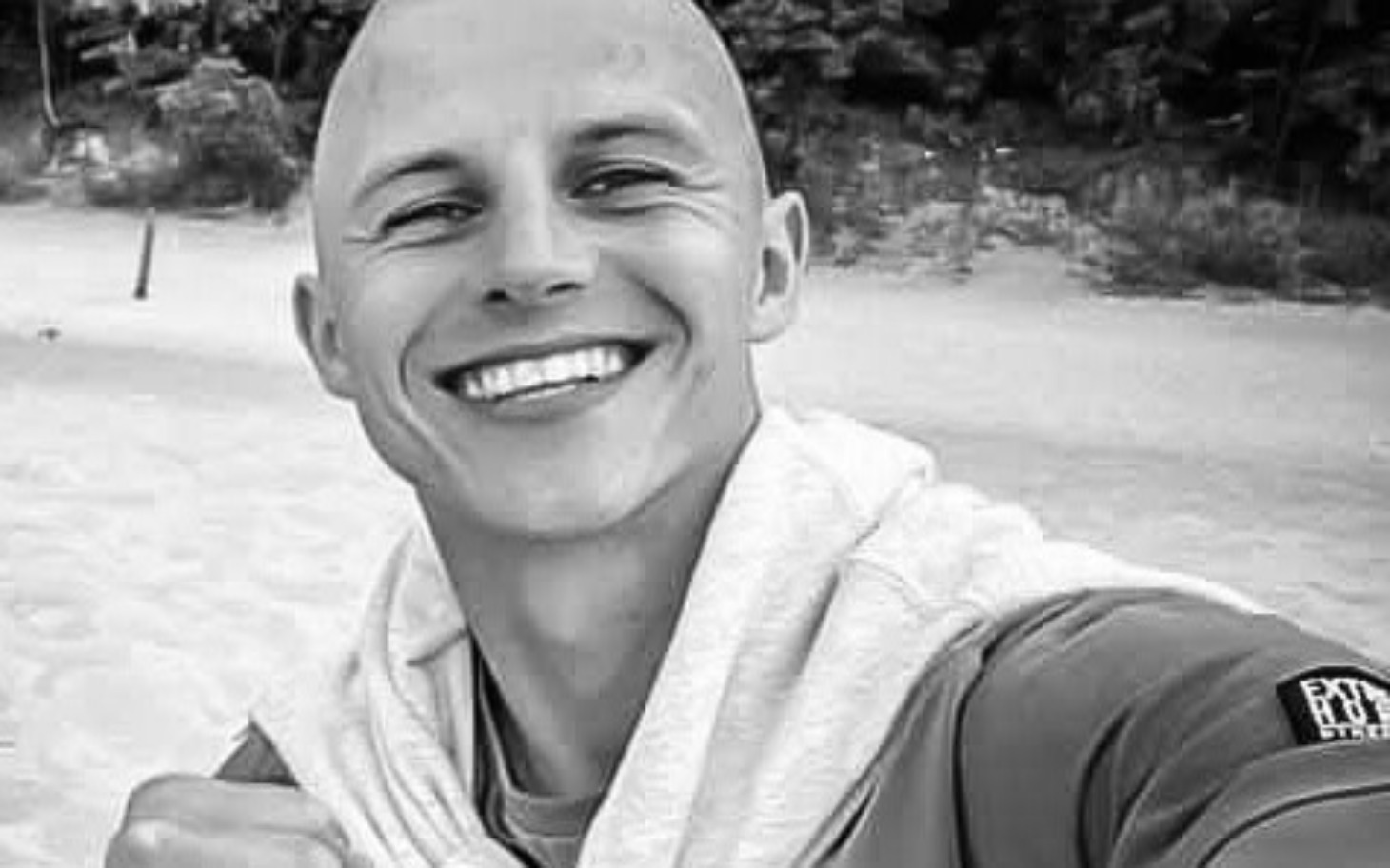 
        Mężczyzna z uśmiechem na plaży, w szarej bluzie, cieszy się chwilą.
    