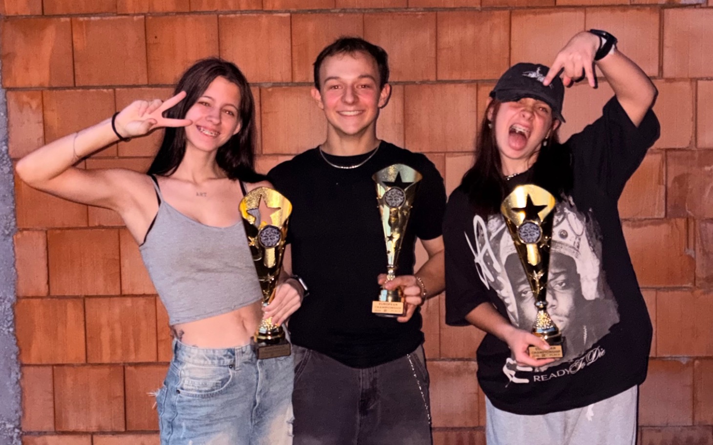 
        Trójka młodych ludzi z trofeami, uśmiechnięci i radośni.
    
