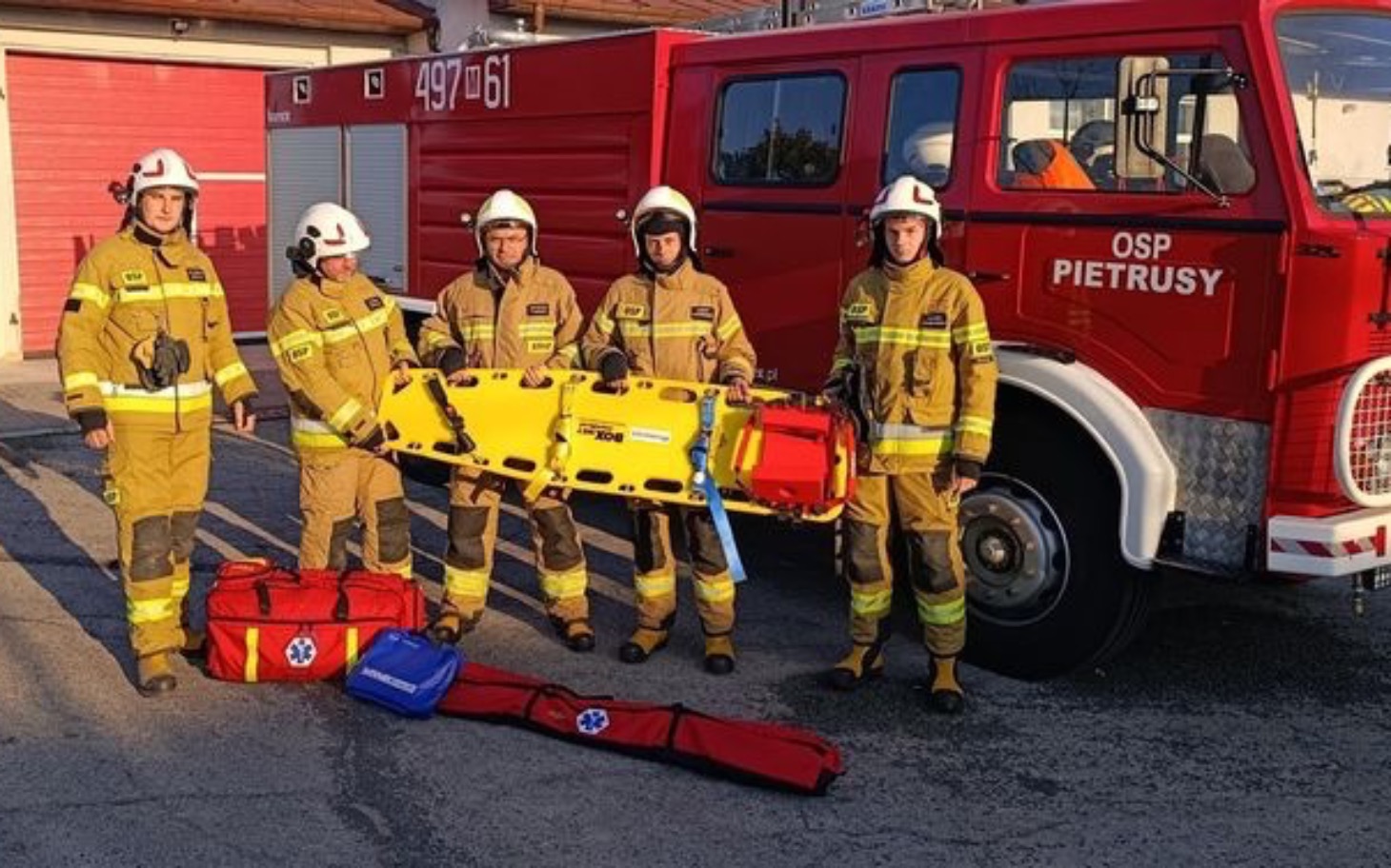
        Grupa strażaków w mundurach obok wozu strażackiego.
    