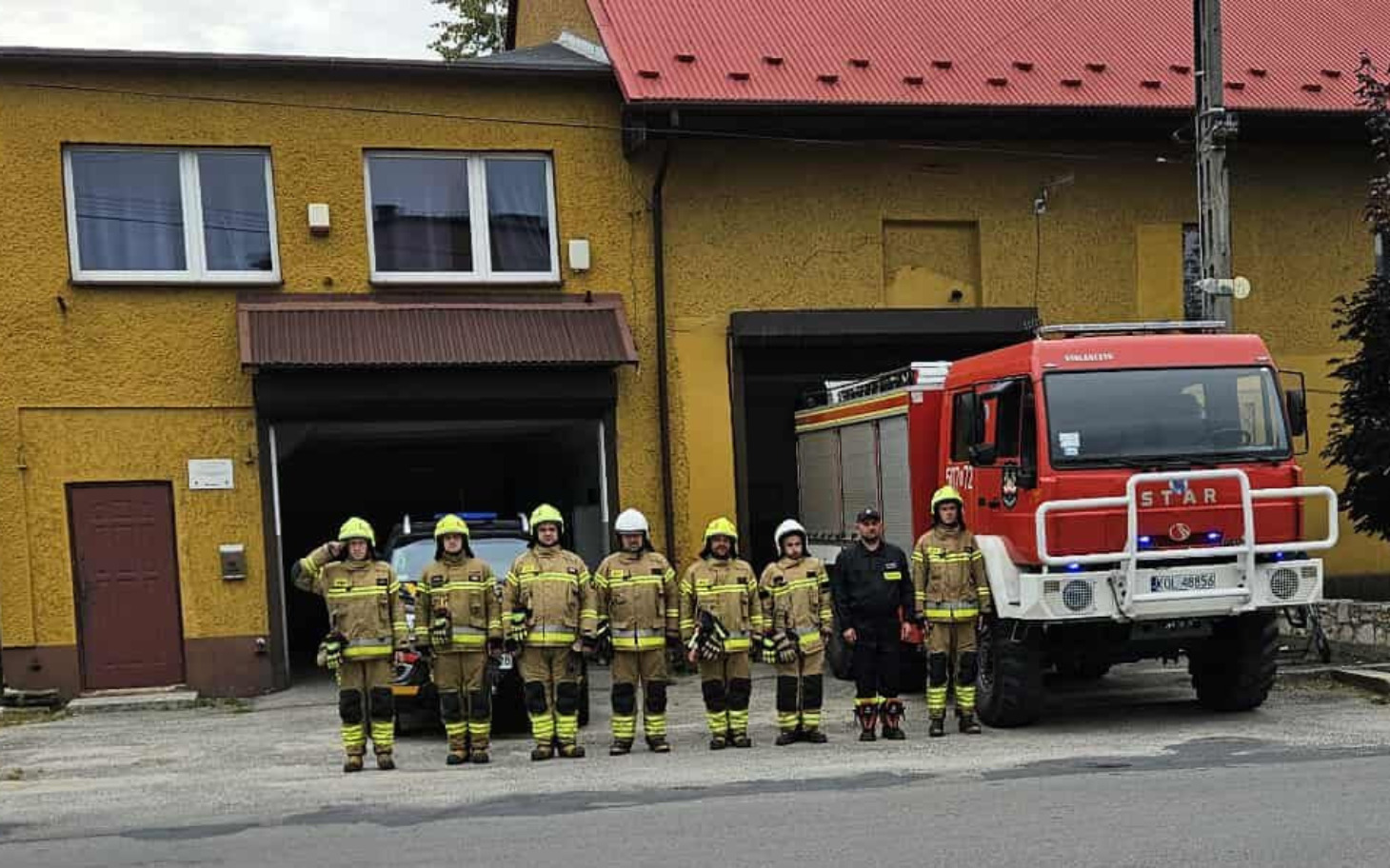 Grupa strażaków przed wozem strażackim.