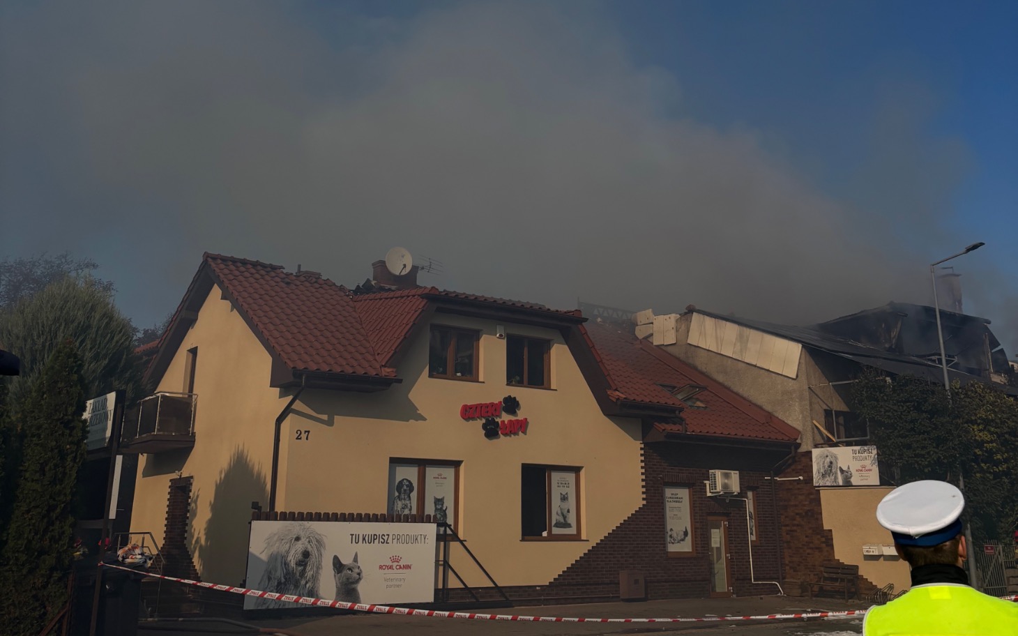 
        Dom z dymem w tle, widać akcję ratunkową.
    