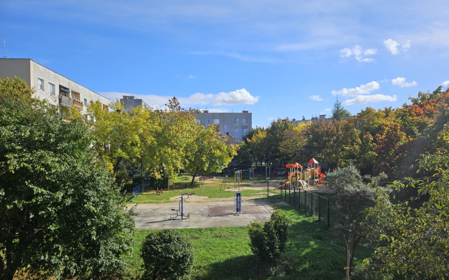 
        Widok na plac zabaw w parku, otoczony zielenią.
    