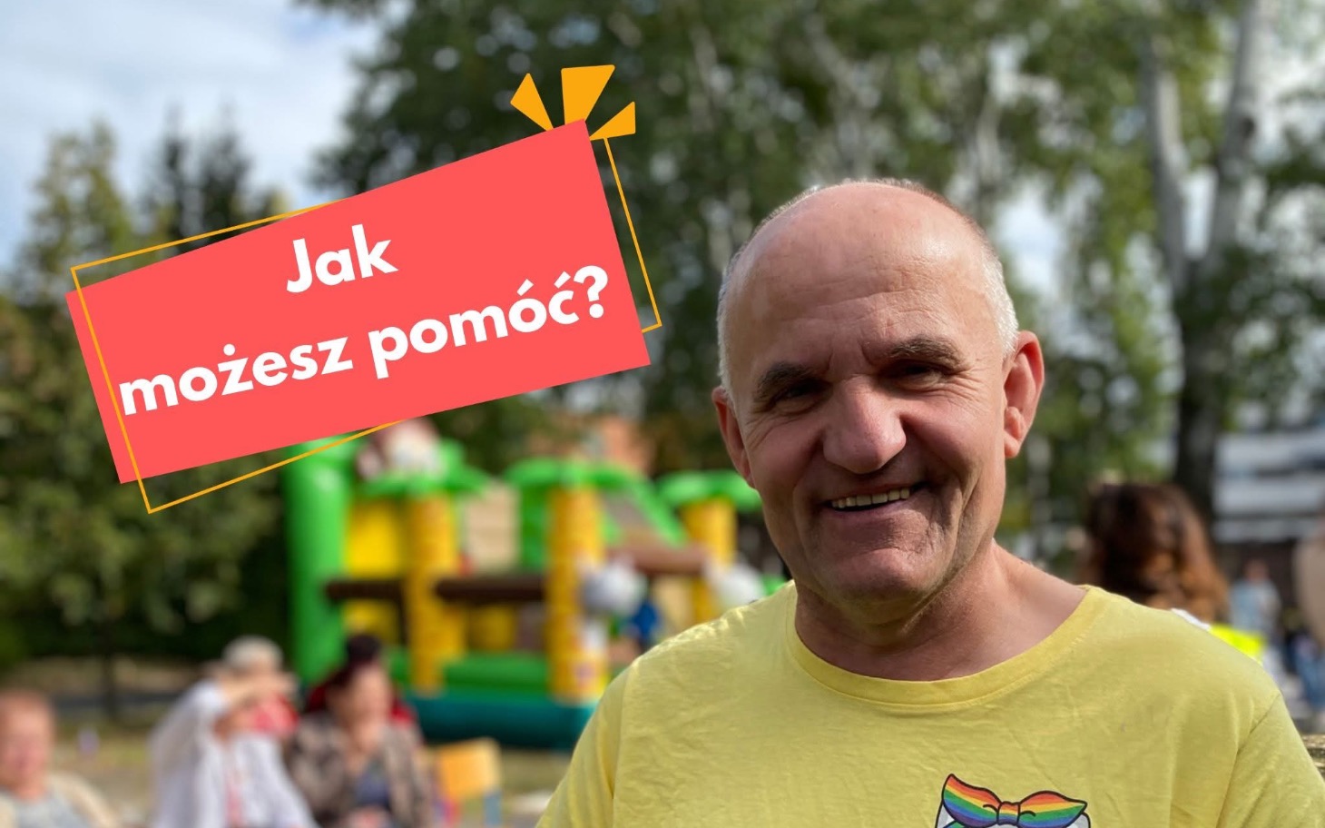 
        Uśmiechnięty mężczyzna w żółtej koszulce na tle placu zabaw.
    