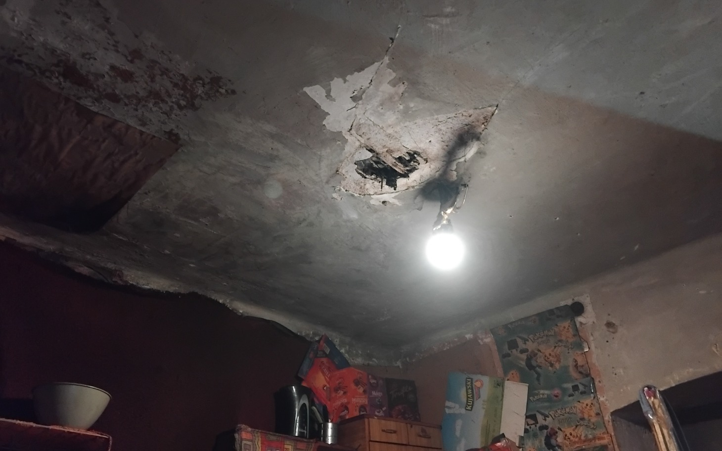 
        Zniszczony sufit w pomieszczeniu z wiszącą żarówką.
    