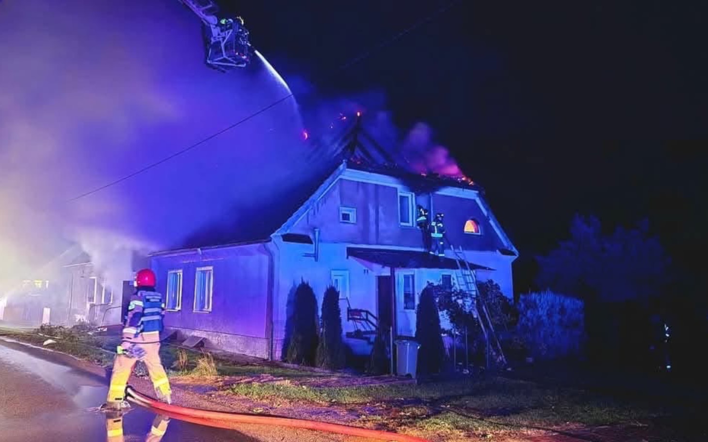 
        Strażacy gaszący pożar w nocy na dachu domu.
    