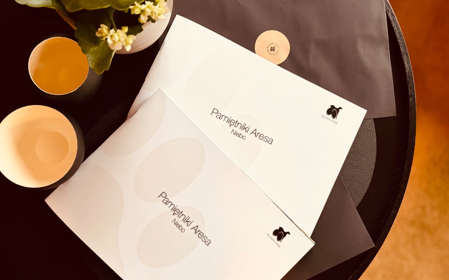 
        Dwa eleganckie foldery na stole, obok kwiaty.
    